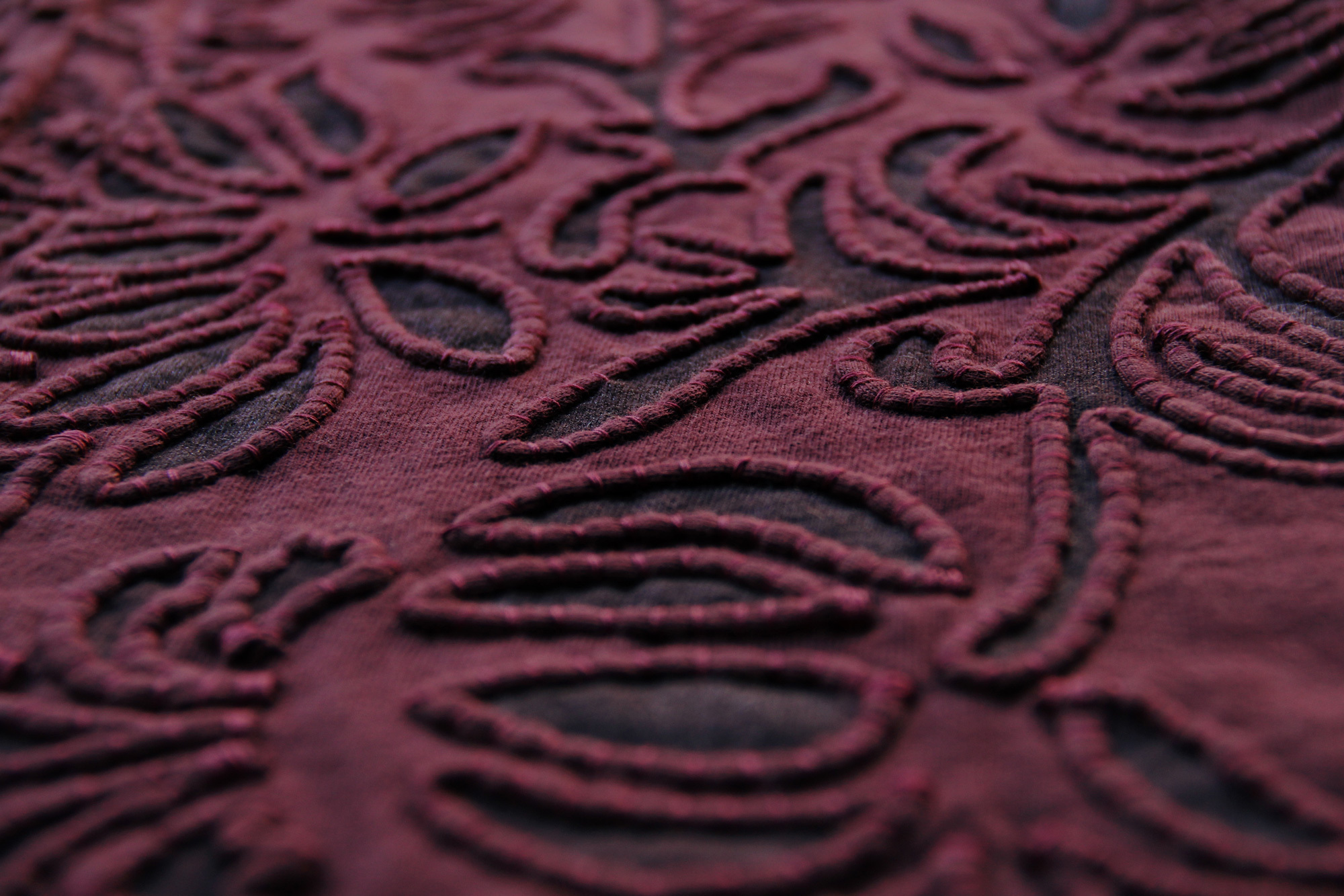 Fabric swatch showing appliqué couching around a floral stencil on plum-colored fabric.